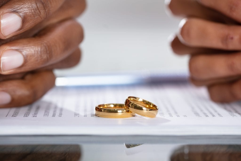 Couple removes wedding bands and signs divorce papers.